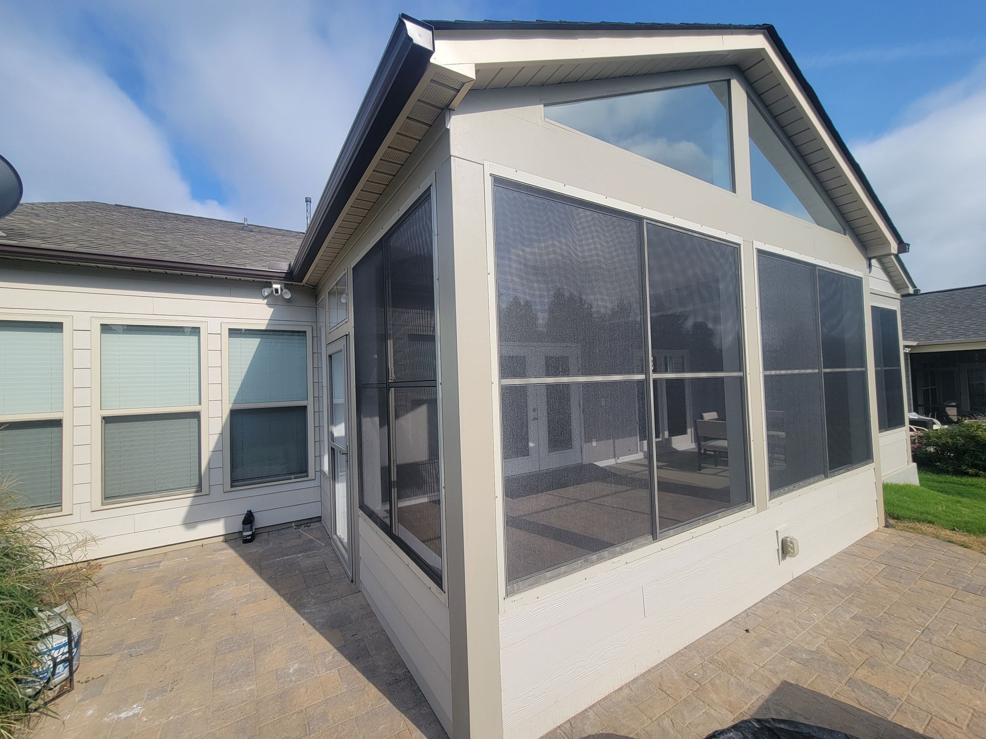 Sunroom with large screened windows attached to a white house under a partly cloudy sky
