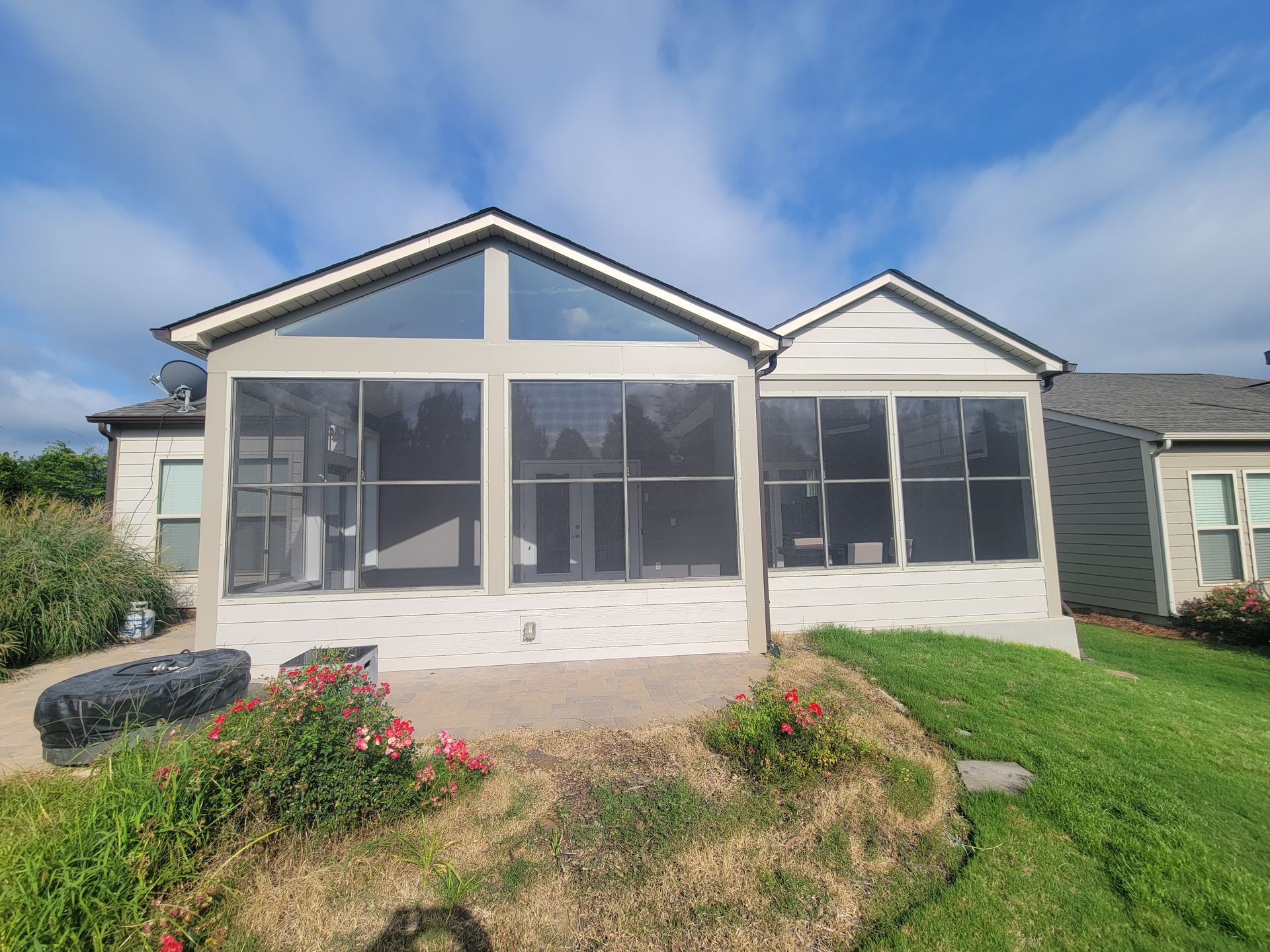 White sunroom addition with screened windows and gabled roof in a grassy yard under a blue sky