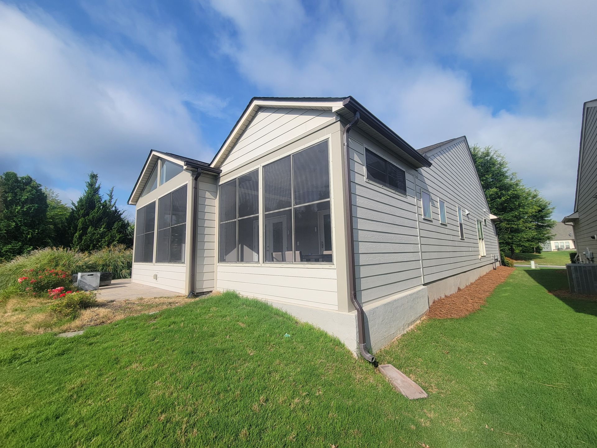 White house exterior with screened porch and grassy sloped yard under a blue sky