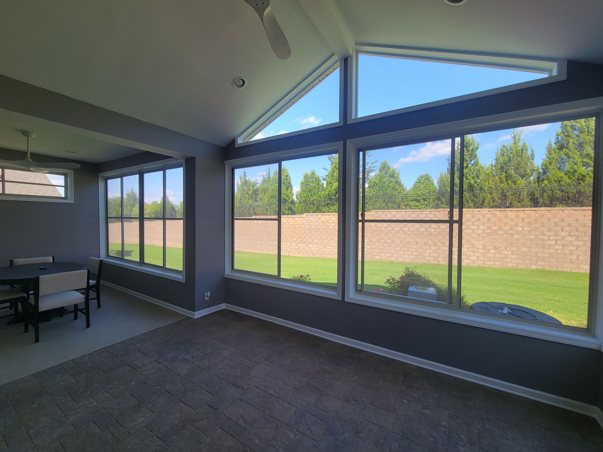 Bright sunroom with large windows, dark carpet, and view of green lawn and brick wall.