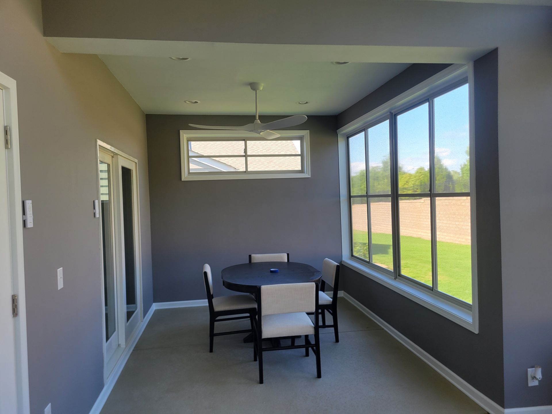 Covered patio with dining table and chairs beside large windows and a view of the yard.