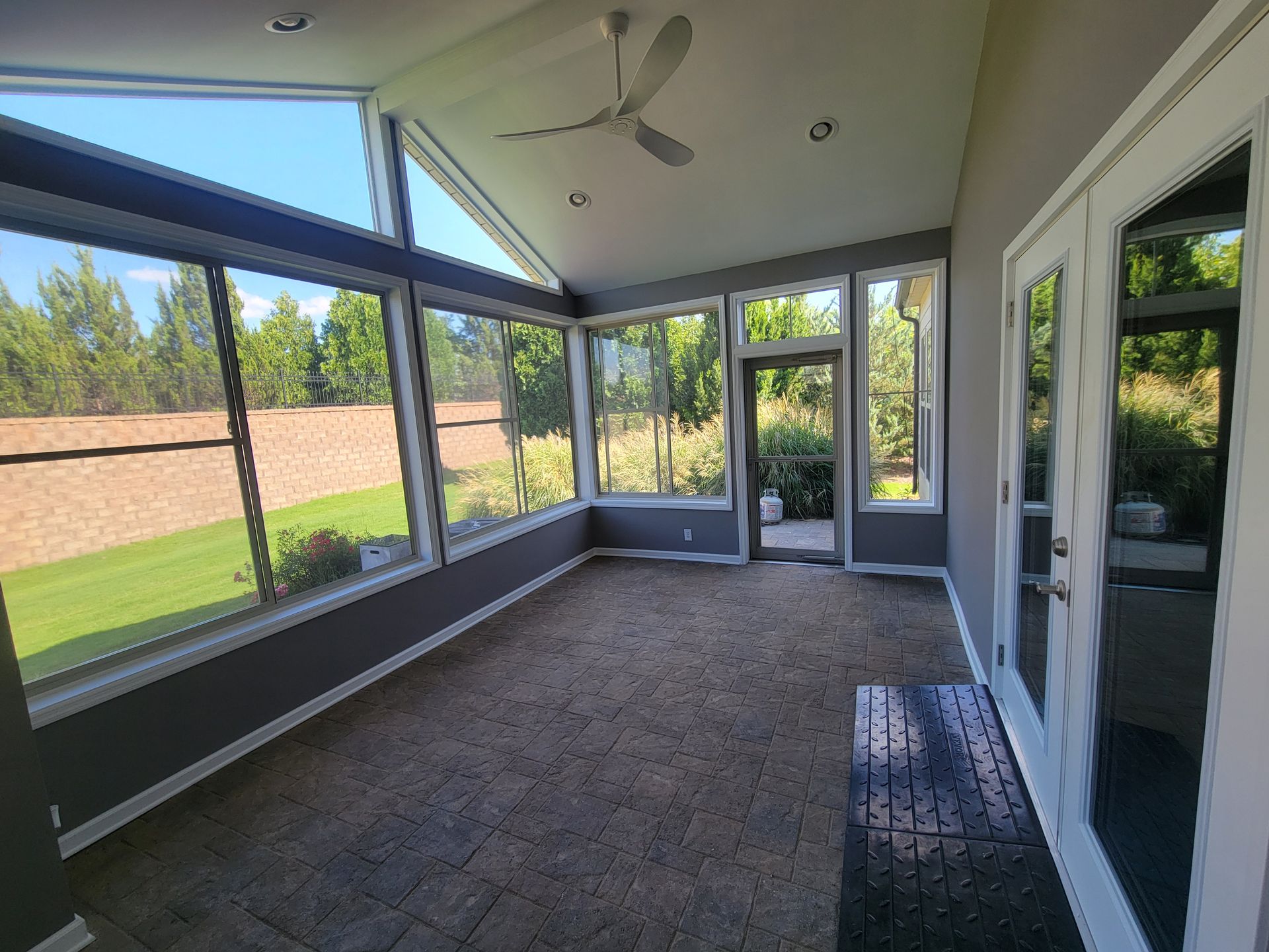 Sunroom with large windows, gray carpet, ceiling fan, and glass doors opening to a fenced yard.