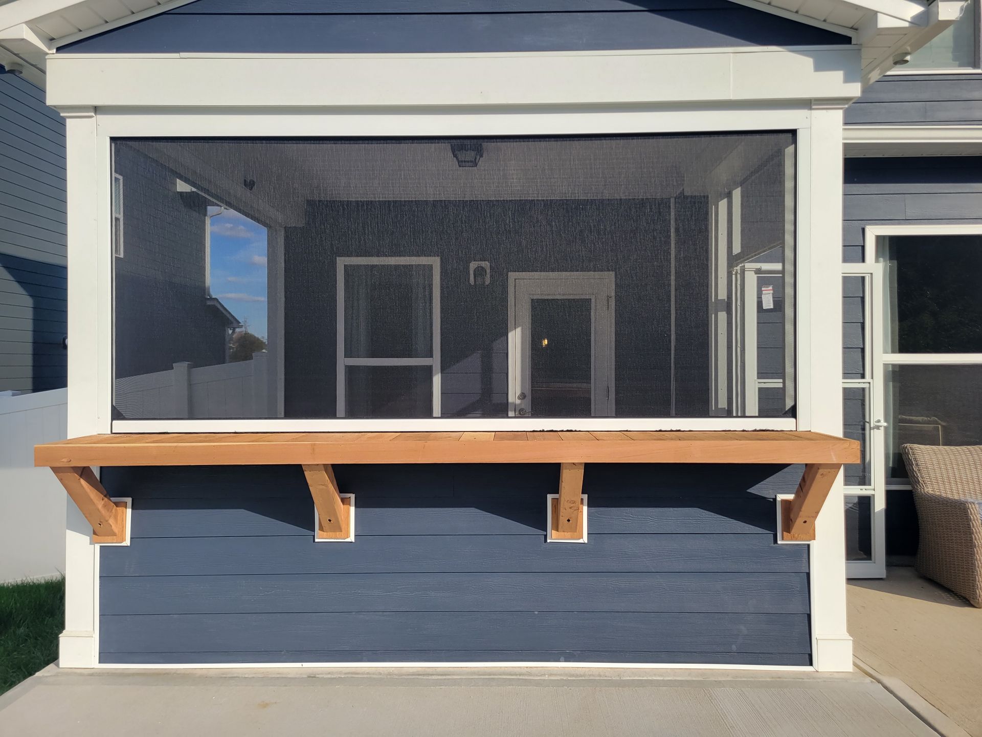 Covered backyard porch with a screened-in sitting area and blue lower wall behind a wooden railing.