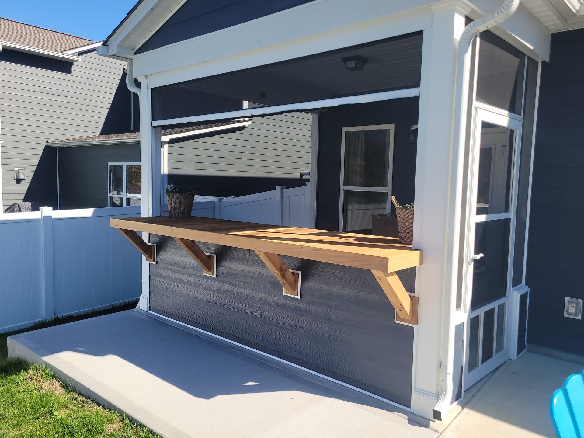 Gray backyard patio bar with a wood counter and open serving window under a roofed porch