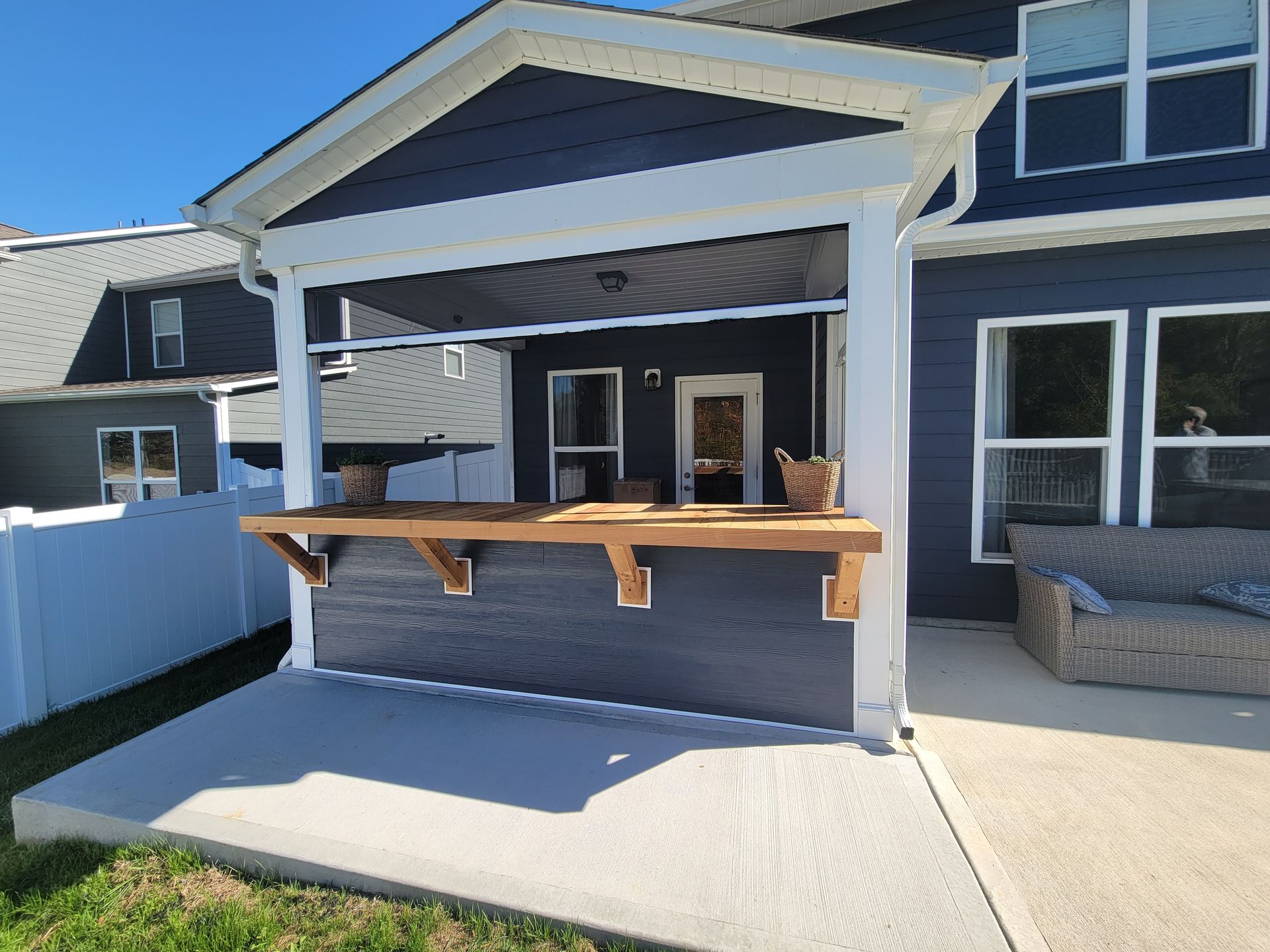 Covered backyard porch with blue siding, wood railing, and a light concrete patio.