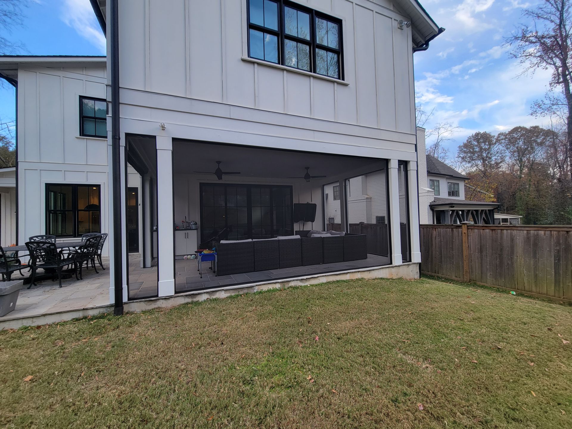 Two-story white house with a screened porch and grassy backyard under a partly cloudy sky