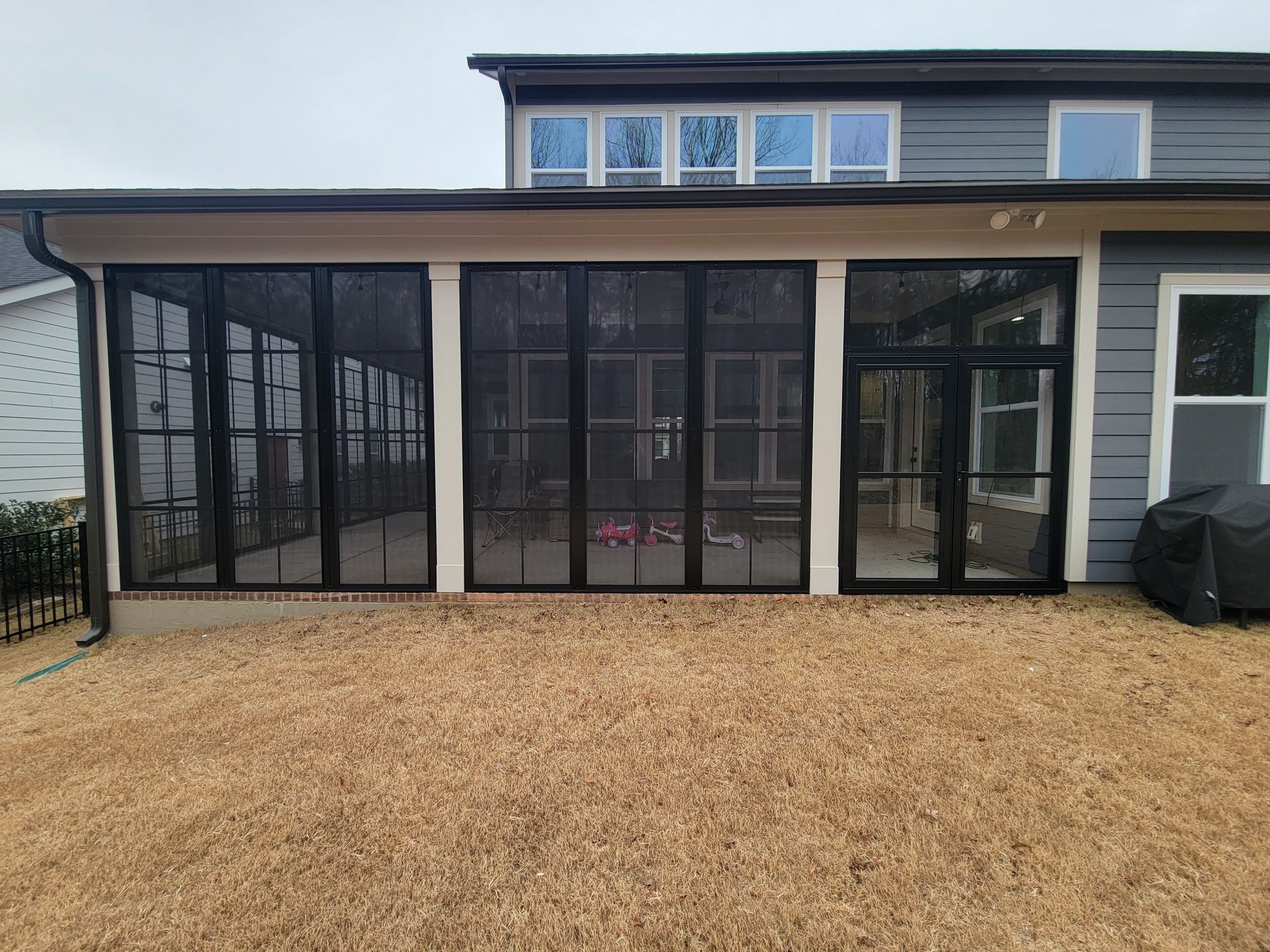 Backyard patio with black-framed glass doors and windows on a modern house, beside a dry lawn