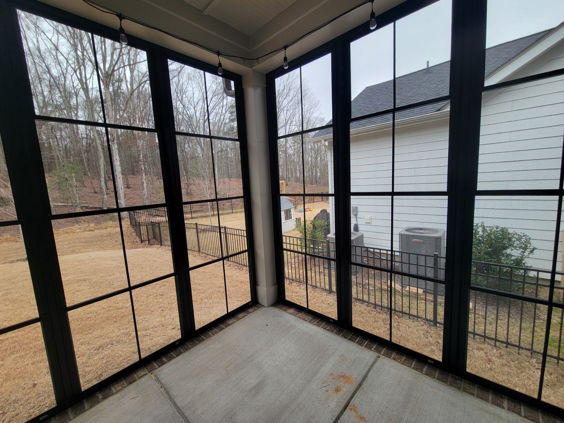 Screened porch with black mesh panels overlooking a yard and neighboring white house.