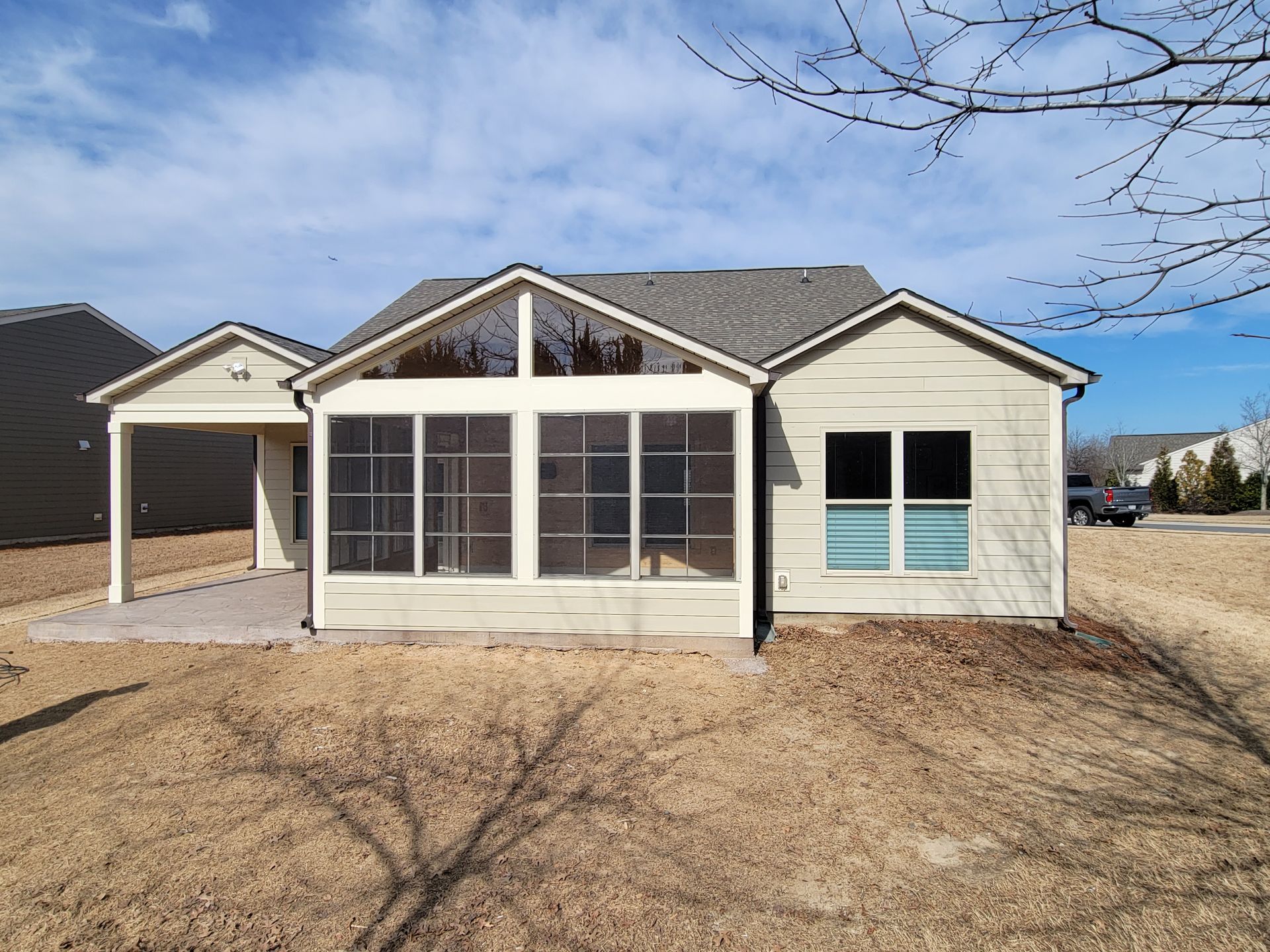 Single-story beige house with a covered front porch and screened windows under a blue sky