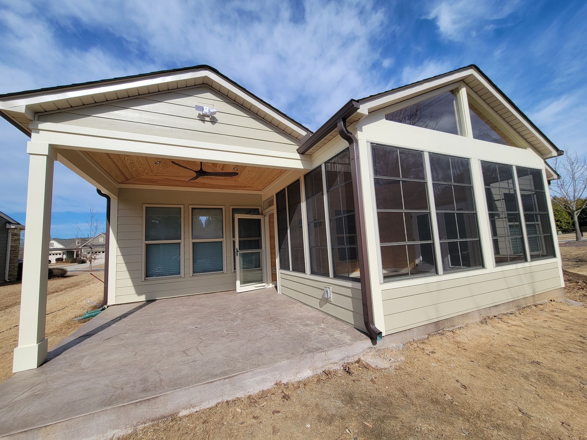 Front view of a beige house with screened porch, concrete walkway, and dry yard under a blue sky