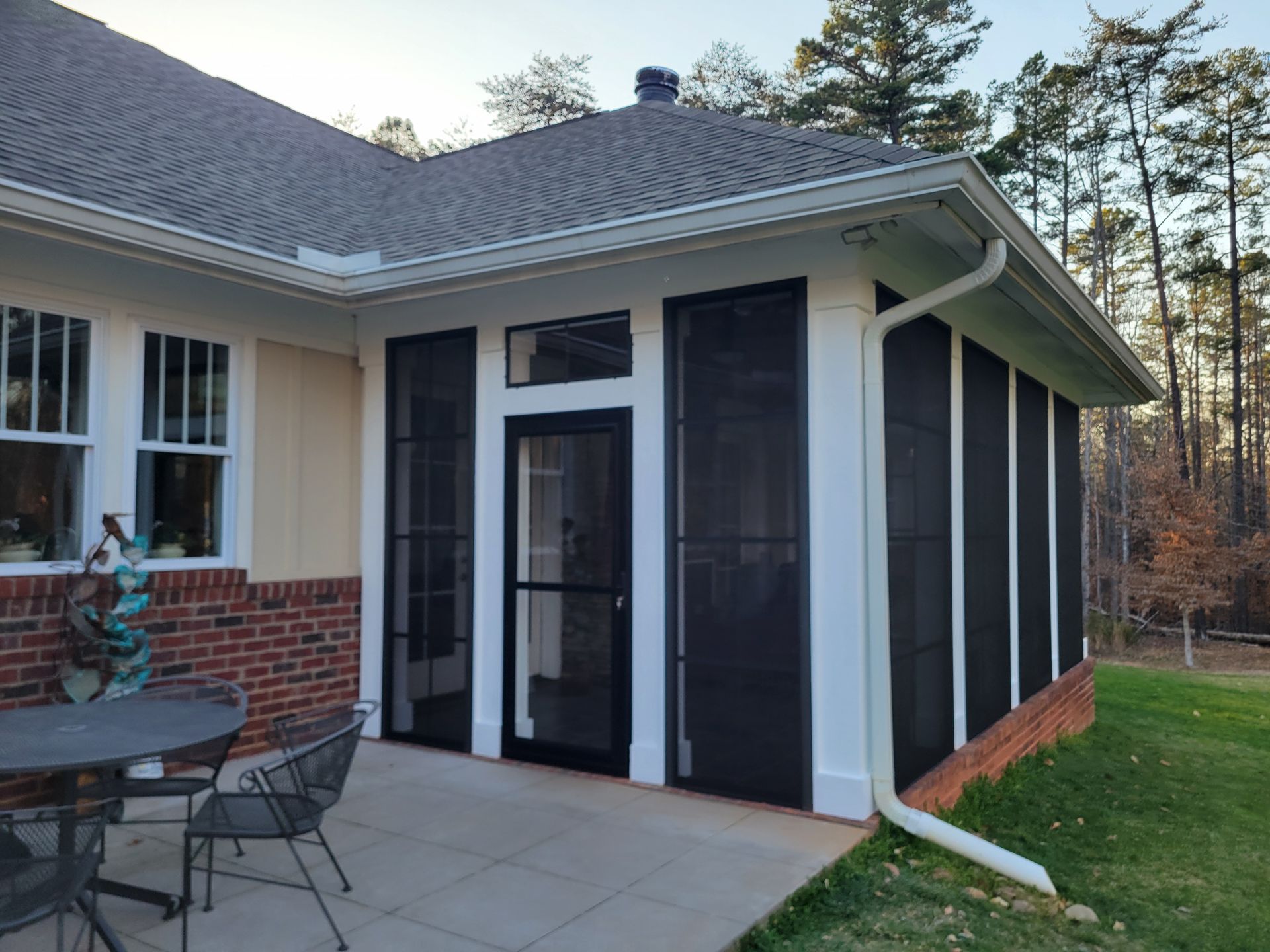 Patio corner of a house with glass doors, dark window shades, and a brick wall beside outdoor furniture