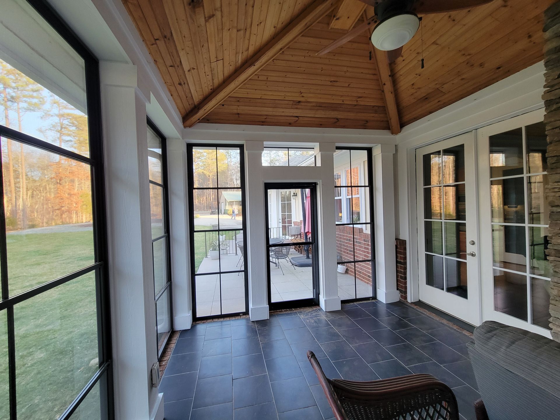 Sunroom with wood-paneled vaulted ceiling, black-and-white tile floor, and glass doors opening to a grassy yard