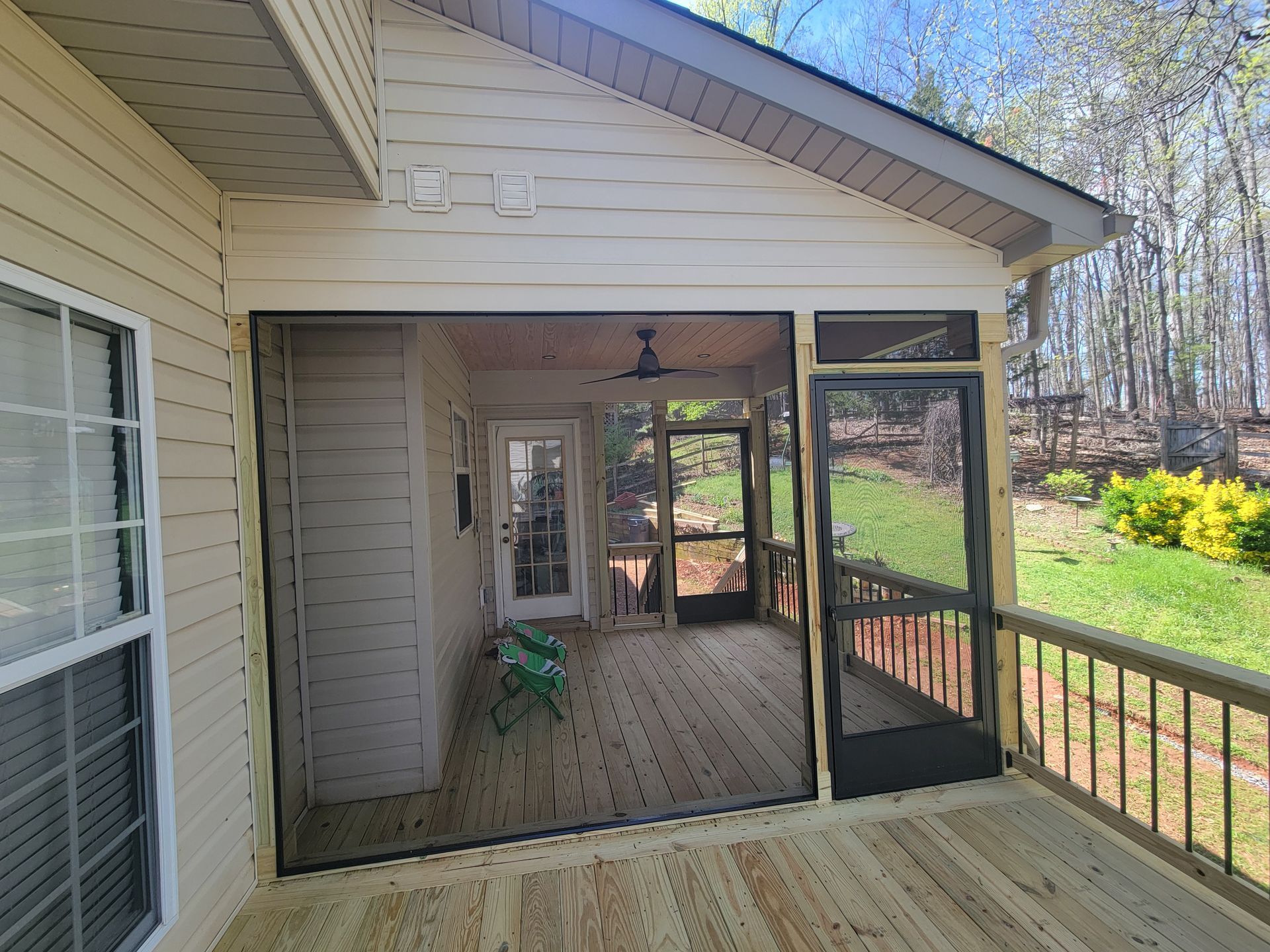 Covered wooden porch with screened seating area beside a house, overlooking a yard and trees.
