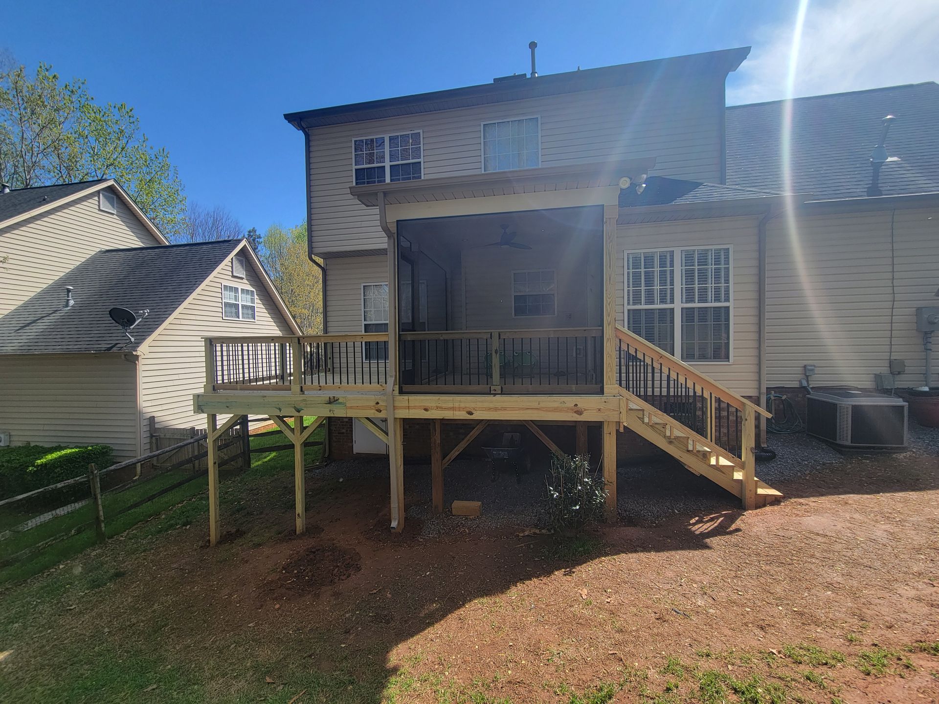 Back deck with stairs on a two-story house, surrounded by a wooded yard.