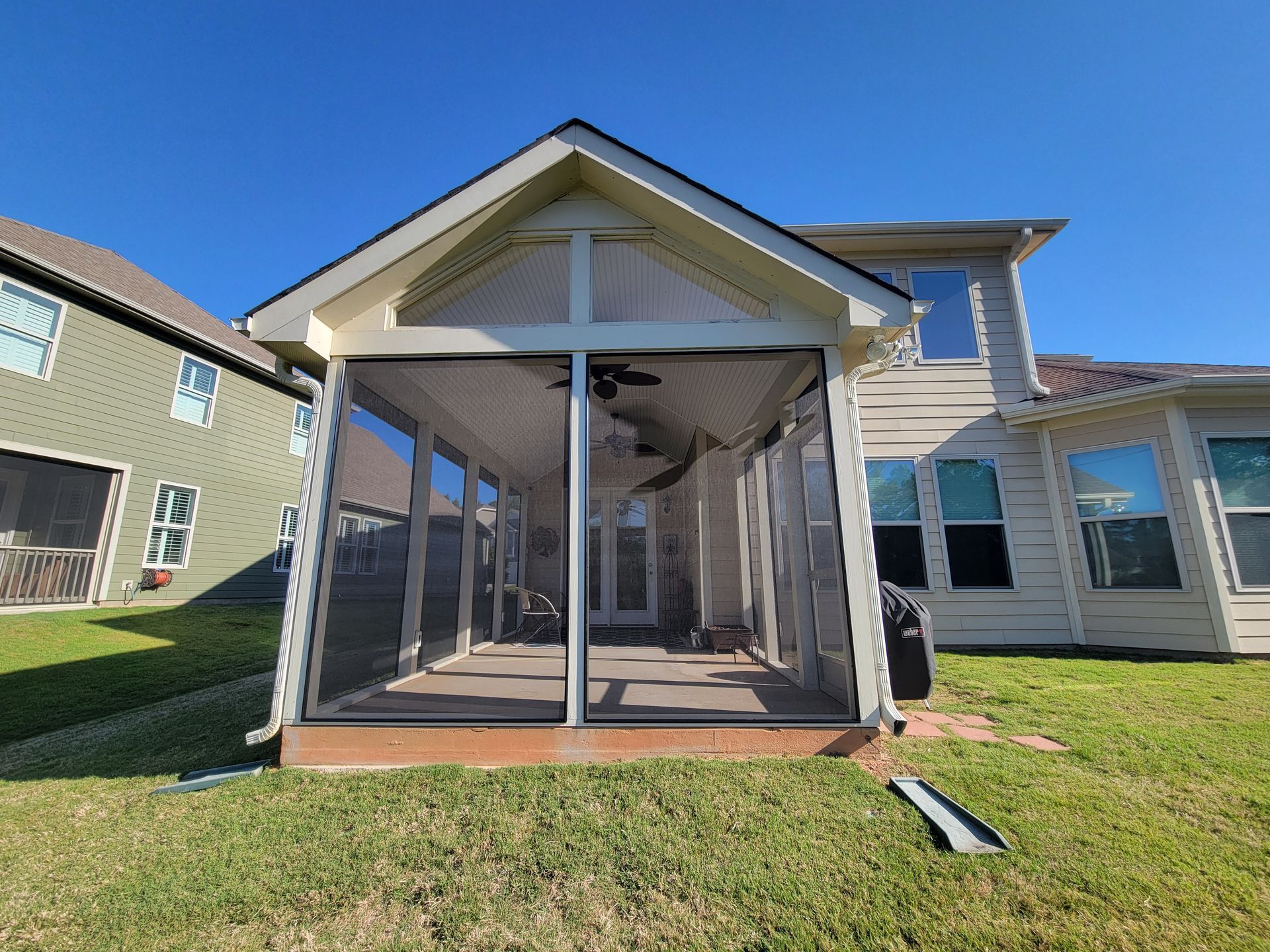 Screened porch with a white gabled roof and sliding glass doors on a suburban house