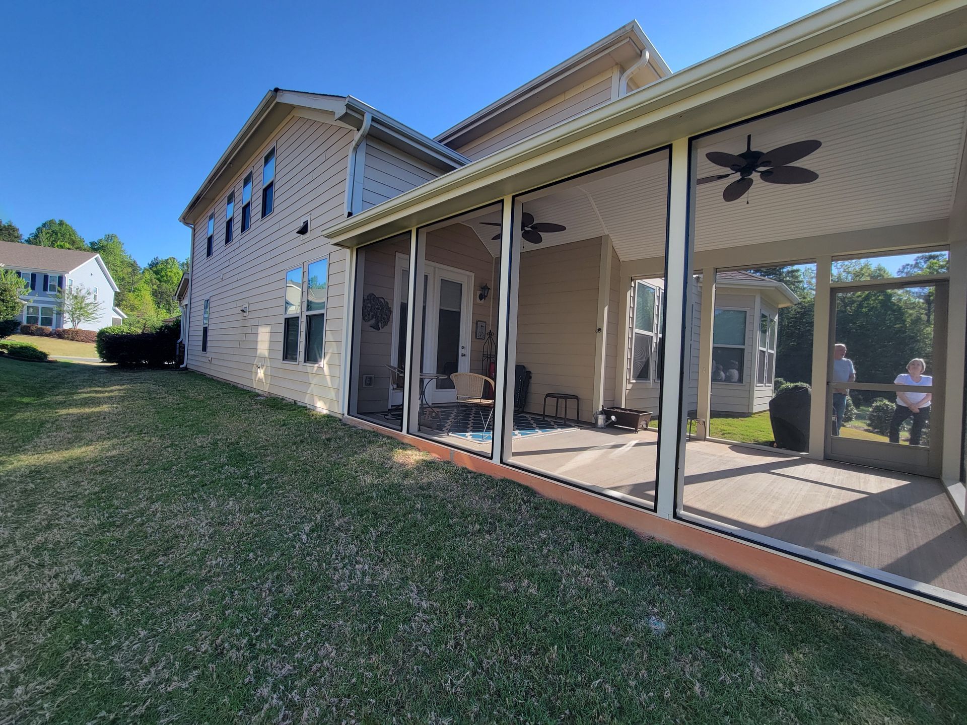 House exterior with screened patio, stone siding, and grassy yard in sunlight