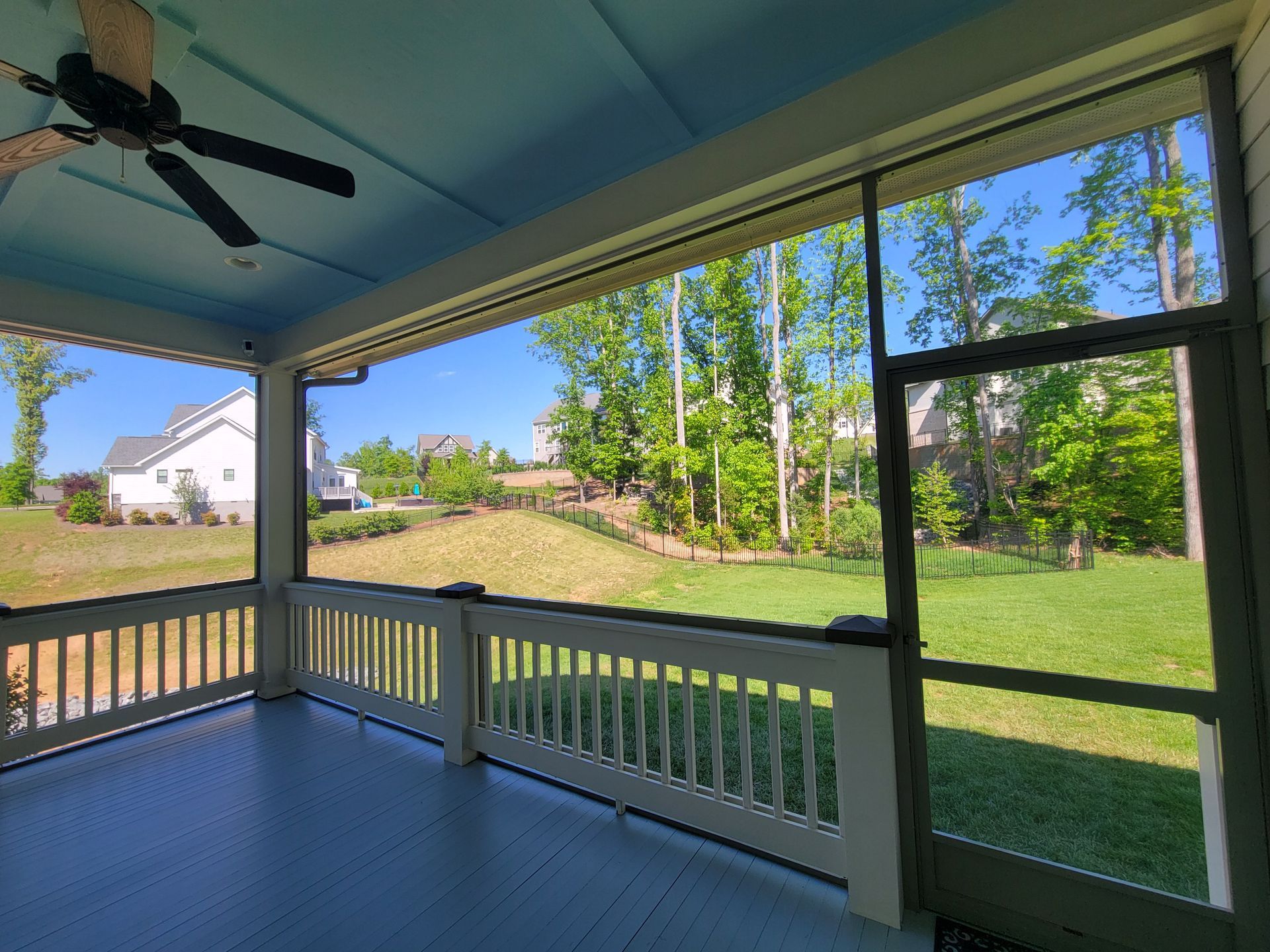 Covered porch overlooking a green yard and trees, with a blue floor and white railing