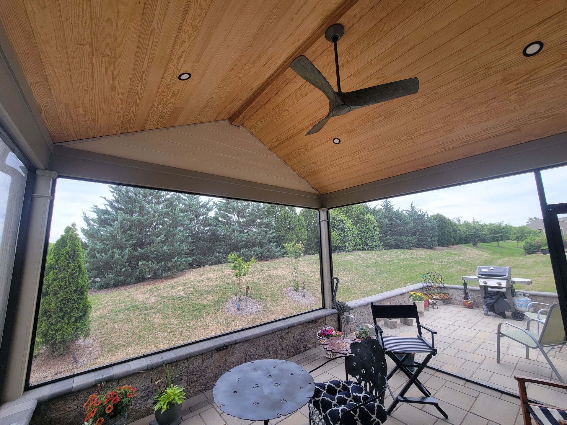Screened patio with ceiling fan, table and chairs, overlooking a grassy yard and trees
