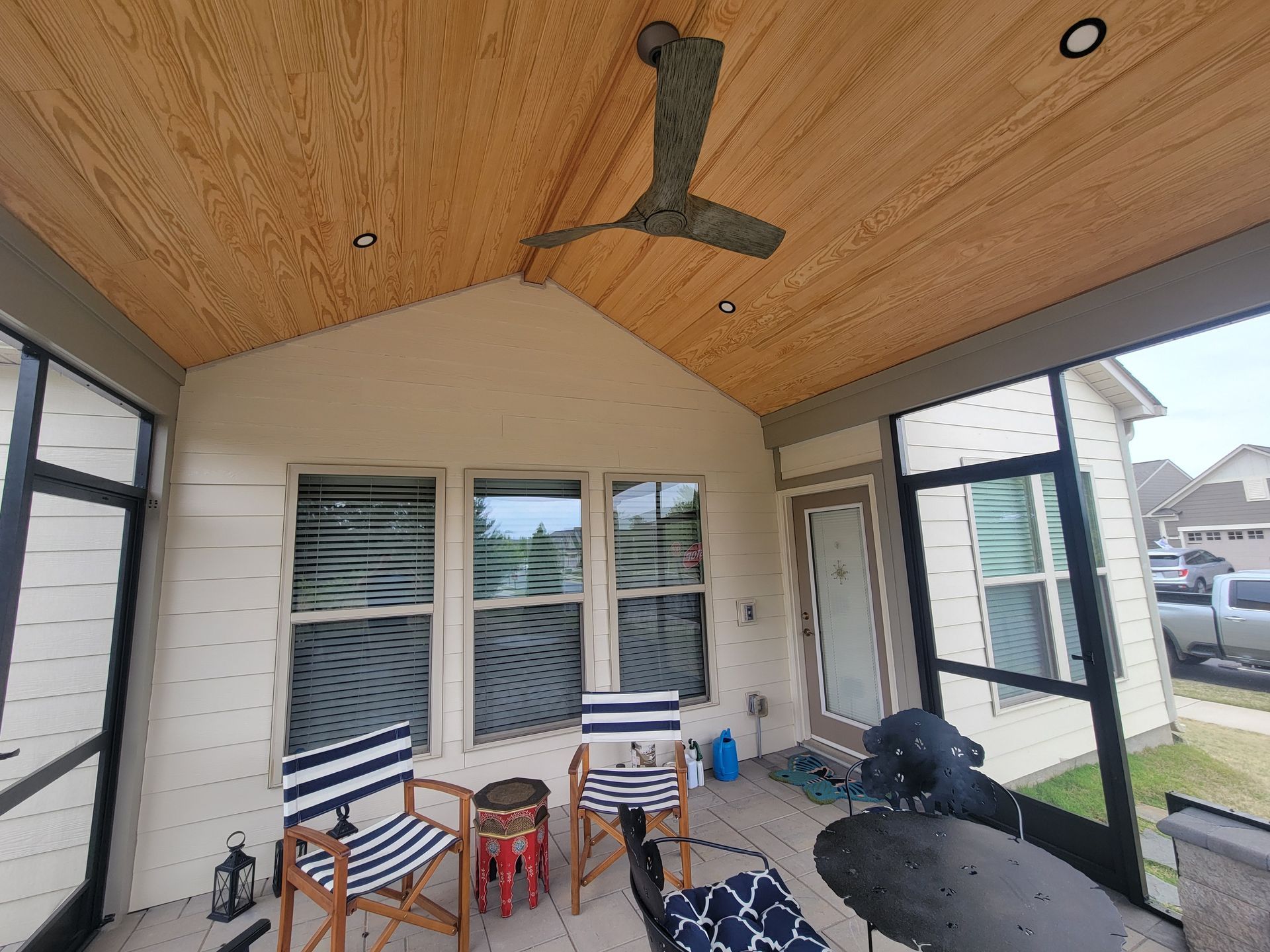 Covered patio with ceiling fan, wicker chairs, small table, and open view to the yard and neighborhood.