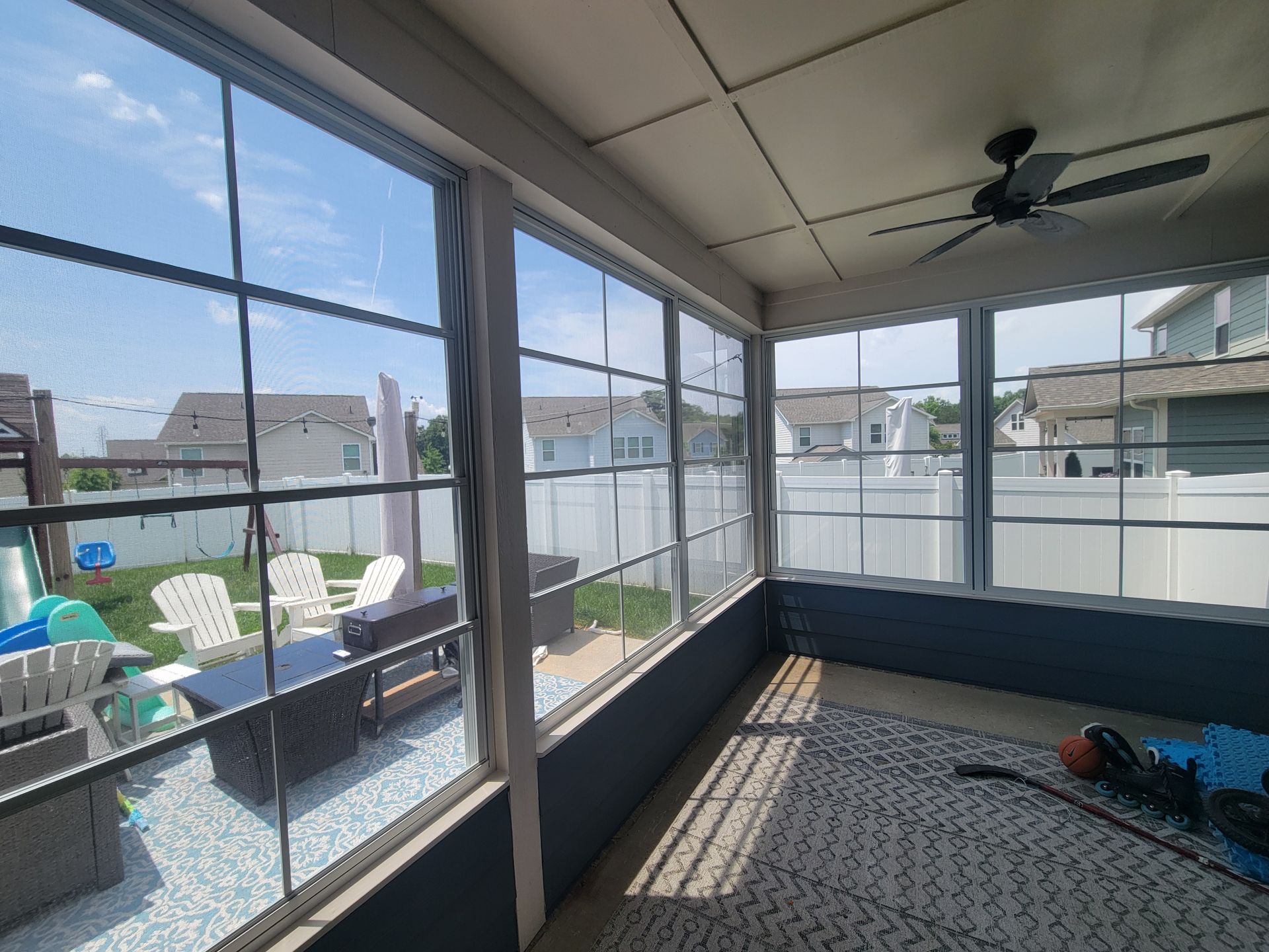Screened porch with large windows, ceiling fan, and patio chairs overlooking a fenced yard