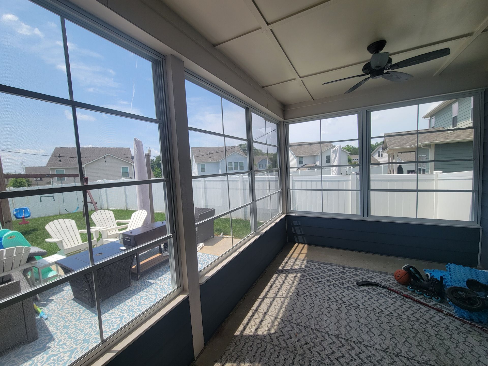 Screened porch with tiled floor, ceiling fan, patio chairs, and a view of neighboring houses and pool.
