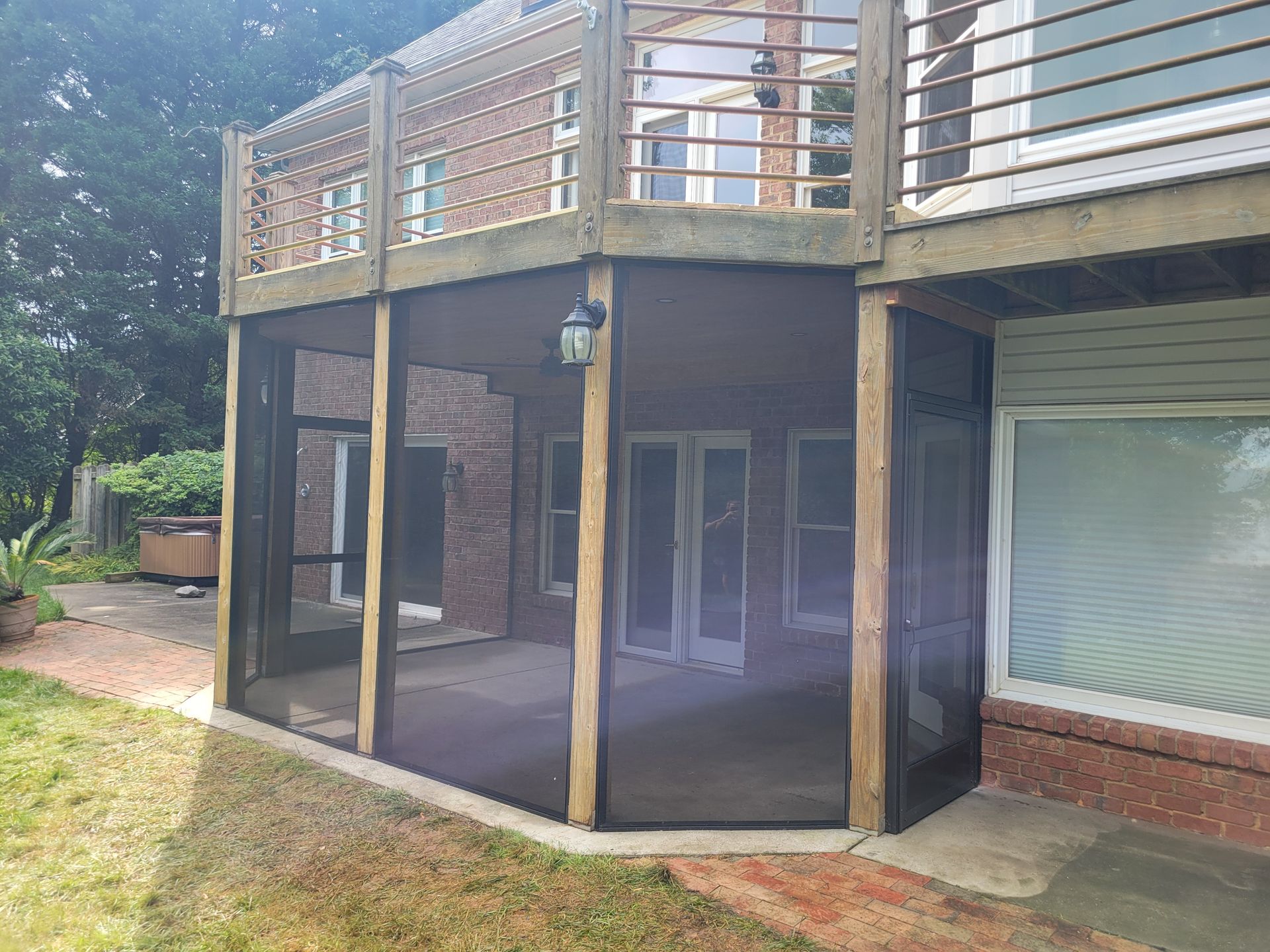 Wooden deck and screened porch attached to a house, with white sliding doors and a sloped lawn.
