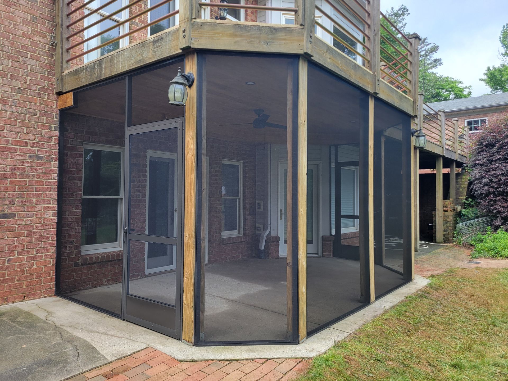 Screened-in porch with dark mesh panels and wooden railings on a brick house