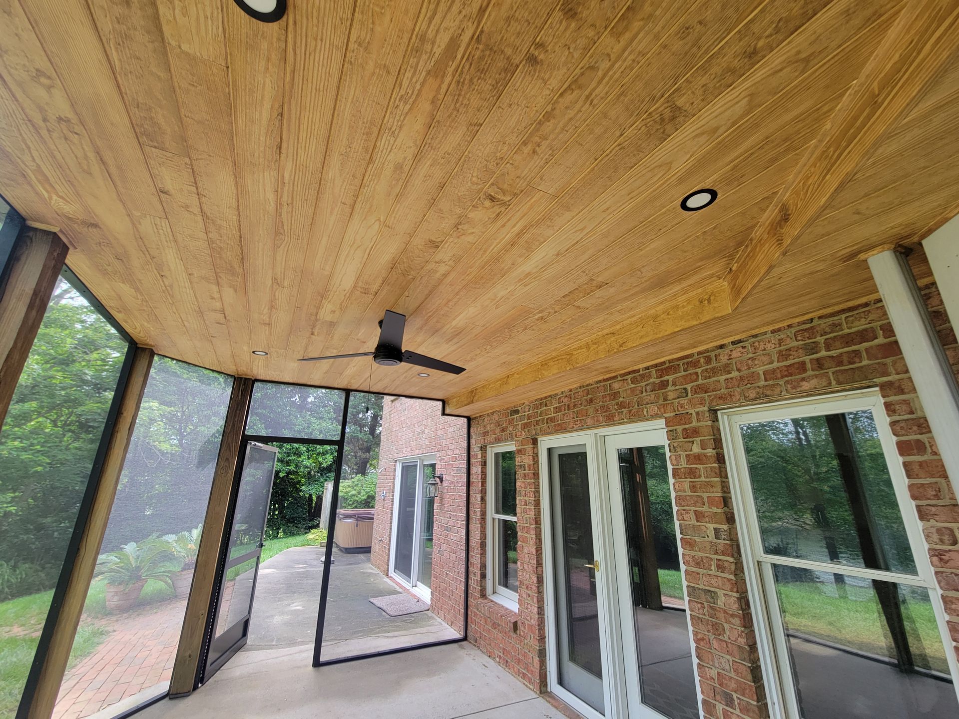 Covered patio with wood ceiling, ceiling fan, brick wall, and sliding glass doors overlooking a yard