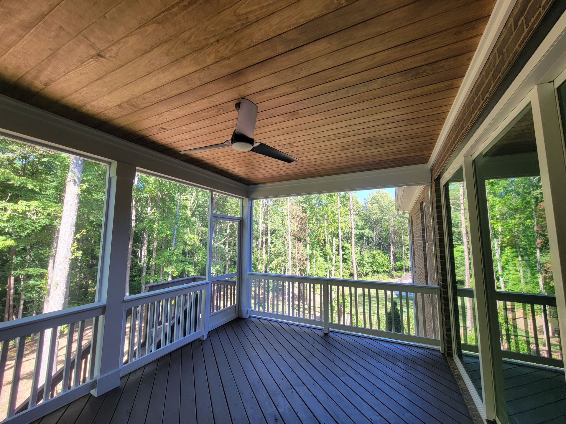 Covered porch with wood ceiling, blue railing, and view of green trees through open screens