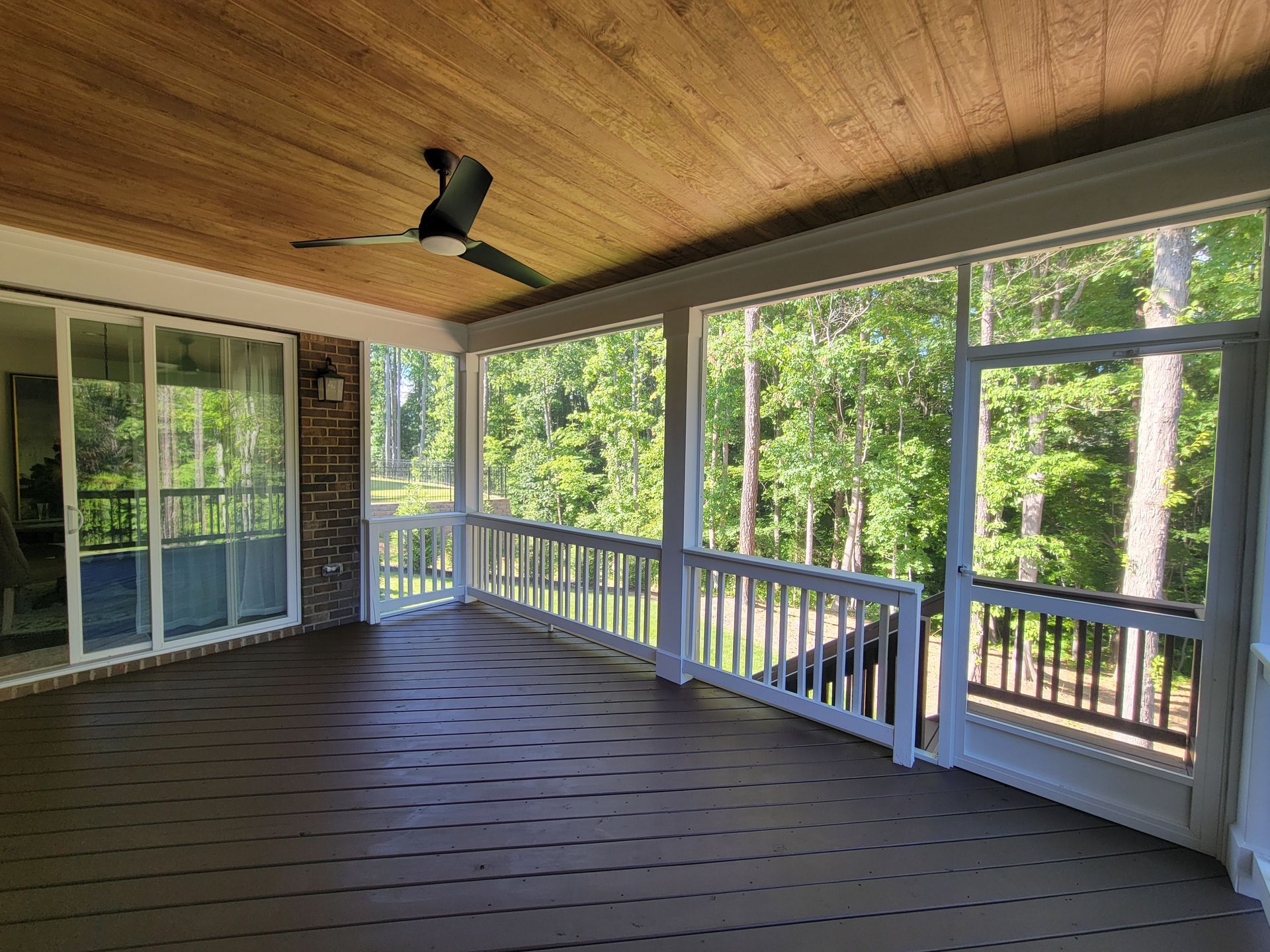 Covered porch with wood ceiling, ceiling fan, white railing, and sliding glass doors overlooking trees