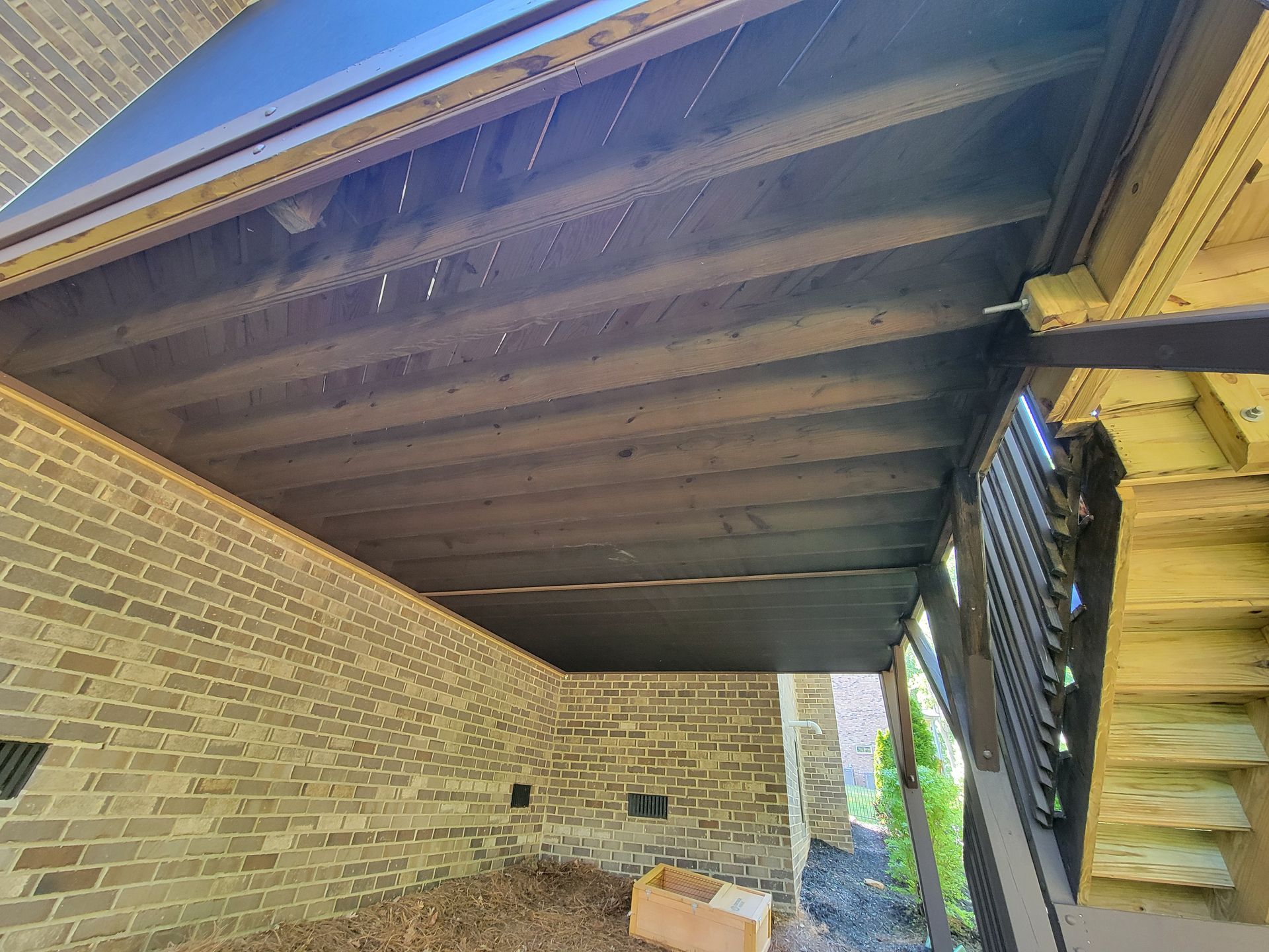 Covered brick patio under a wooden deck, with stairs on the right and a slatted wall at the back.