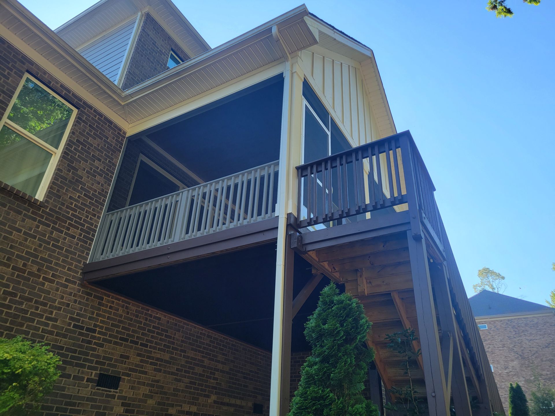 Brick house with a covered porch, white railings, and a staircase under a bright blue sky.