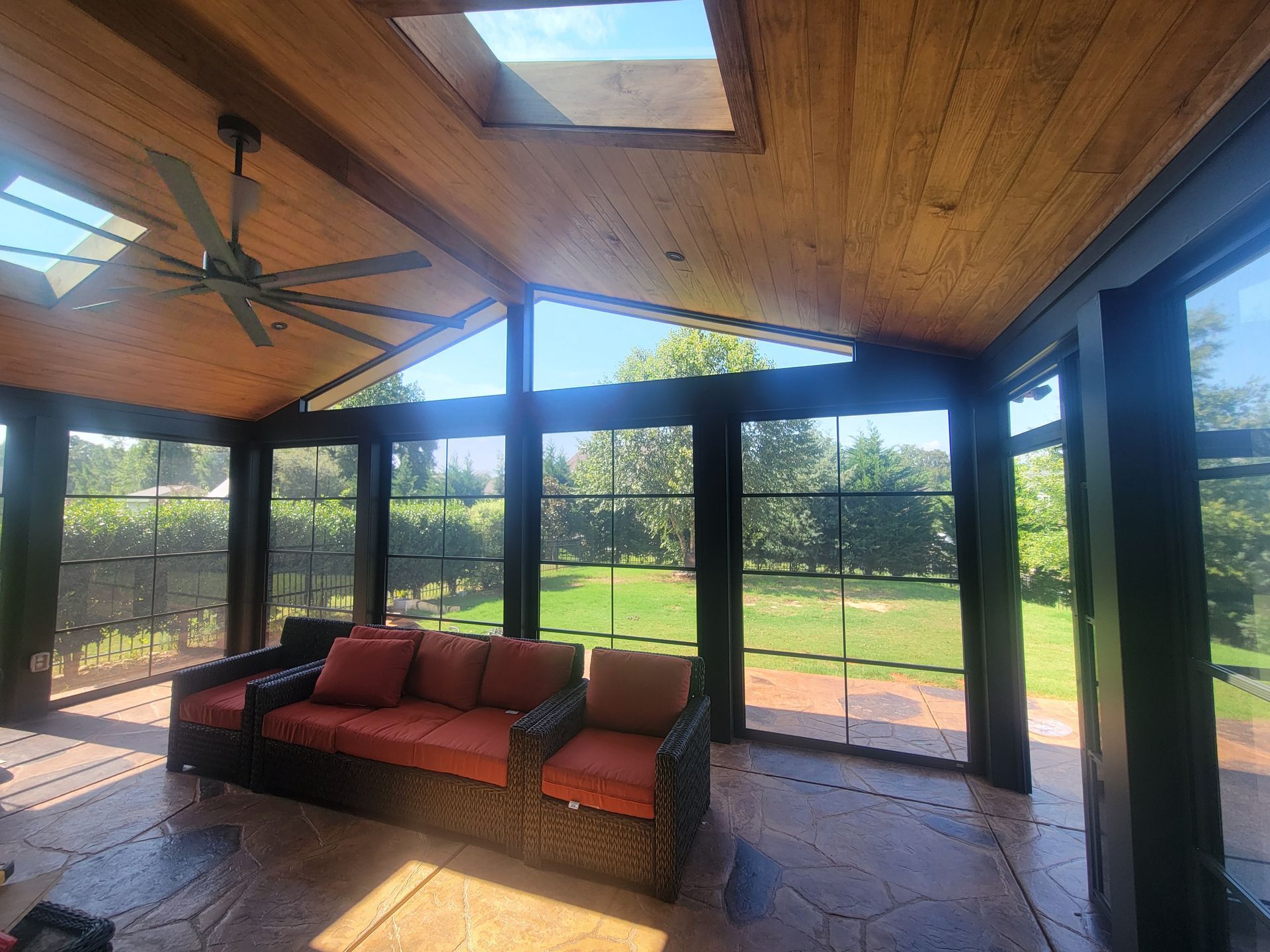 Screened patio with red cushioned sofa, stone floor, wood ceiling, and green yard views