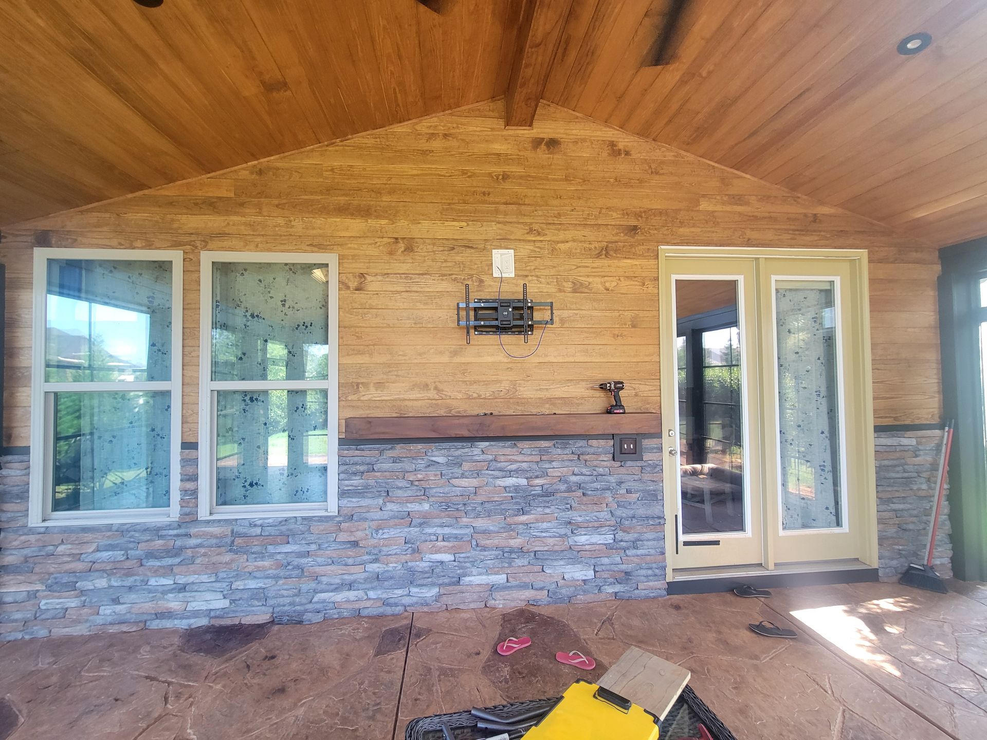 Covered porch with wood-paneled ceiling, stone half-wall, and French doors opening to the outside.