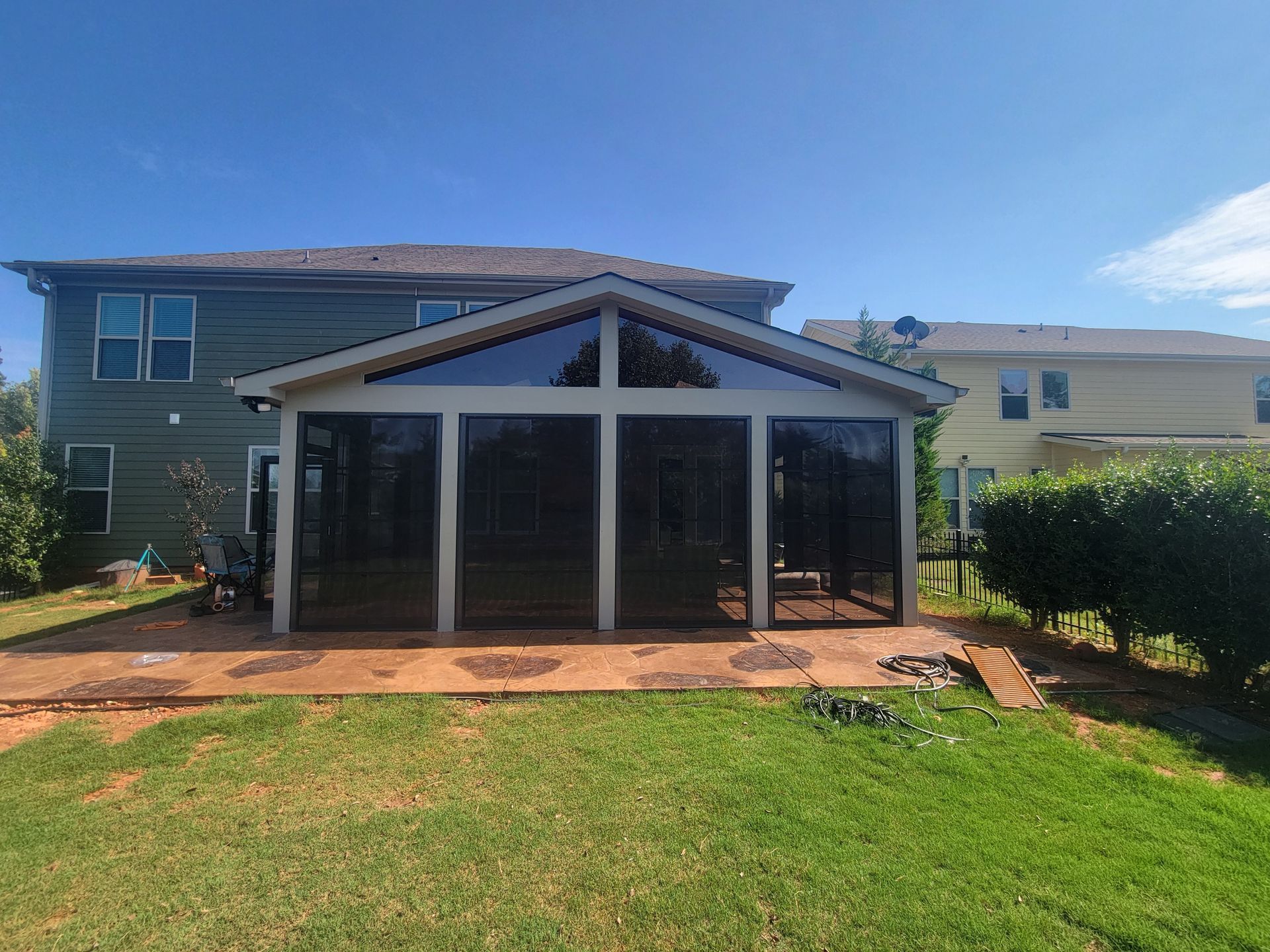 Backyard covered patio with white-framed screened enclosure and lawn, attached to a two-story house