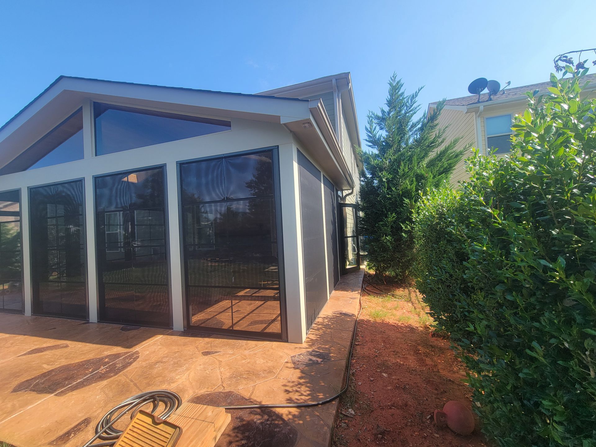 Backyard patio with a screened sunroom, red pavers, and green hedge under a bright blue sky