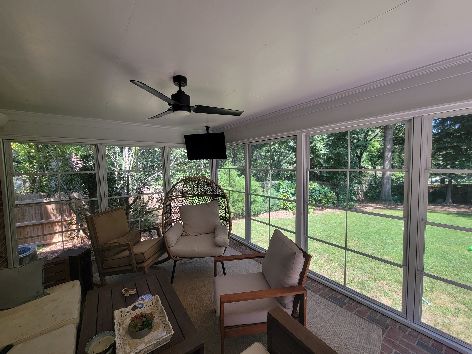 Screened porch with wicker chairs and ceiling fan, overlooking a green backyard.
