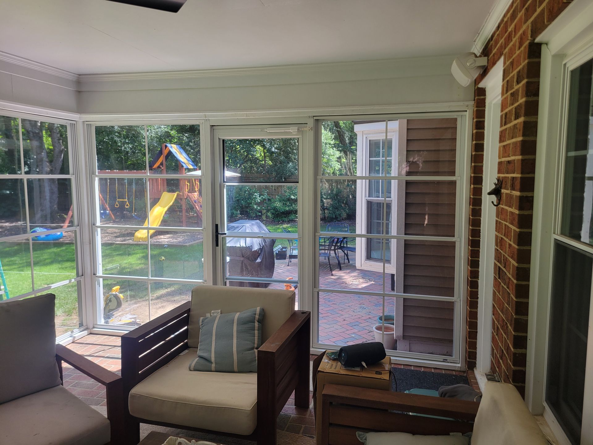 Sunroom with wicker chair and bright backyard view through large windows and glass door.