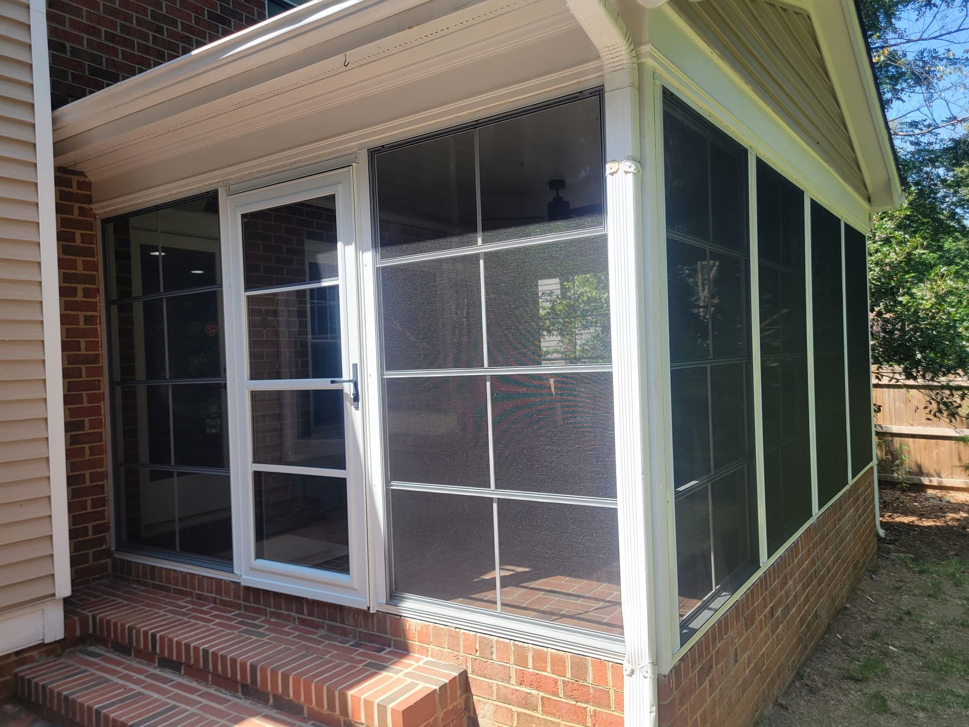 Screened porch with white-framed sliding glass doors and dark mesh panels on a brick base.