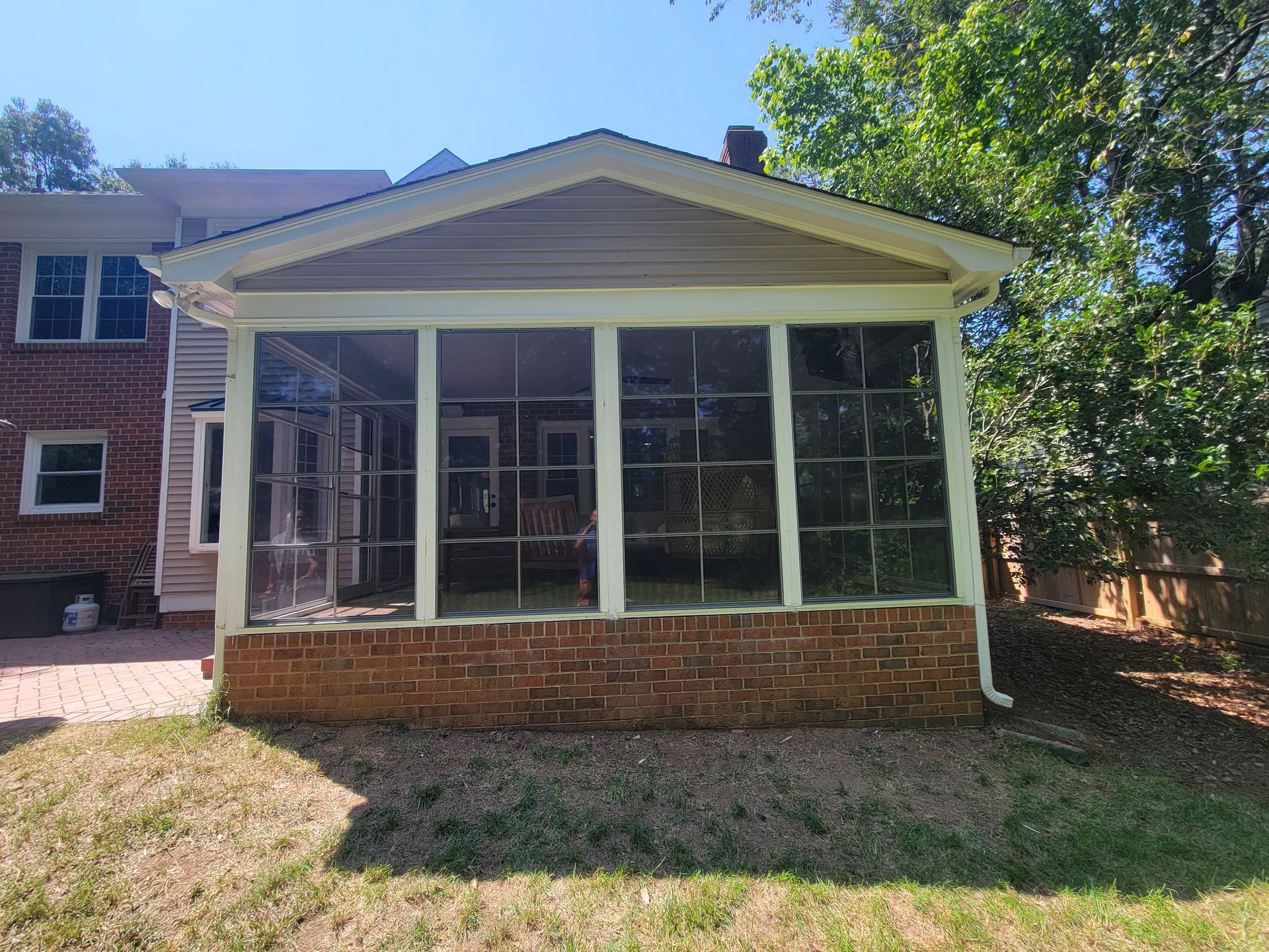 Screened porch with white trim and brick base on a sunny house exterior