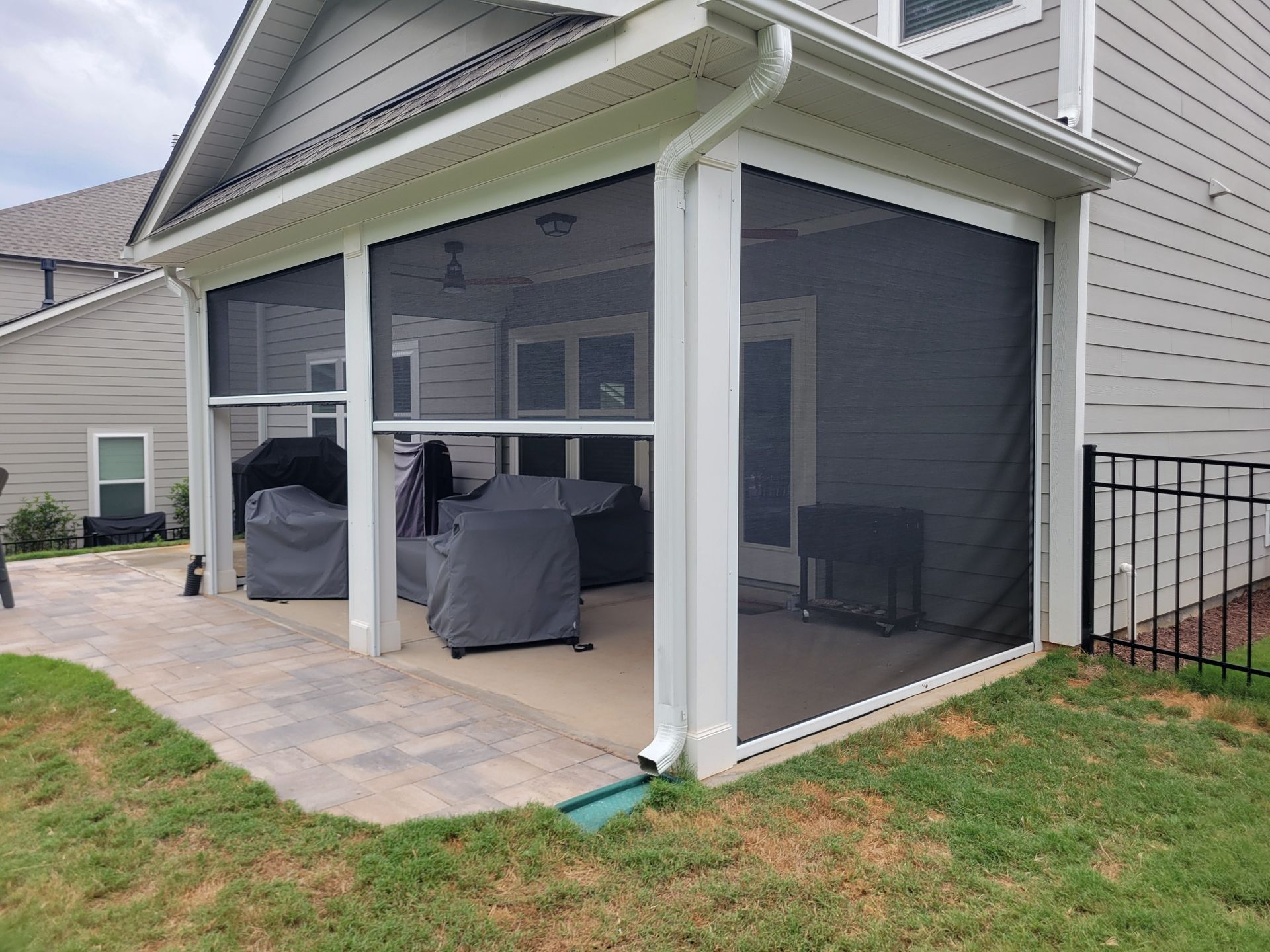 Screened backyard patio with covered outdoor seating beside a house and lawn