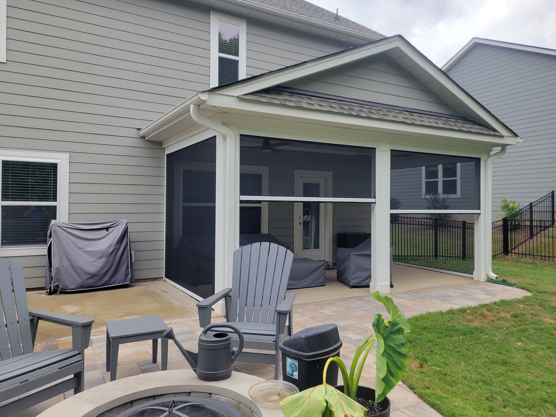 Covered patio with screened enclosure, outdoor furniture, and a grassy backyard beside a gray house