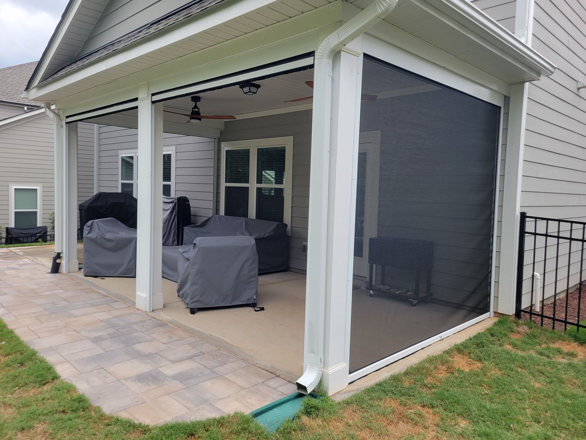 Covered patio with screened side enclosure, outdoor furniture, and paver flooring beside a house