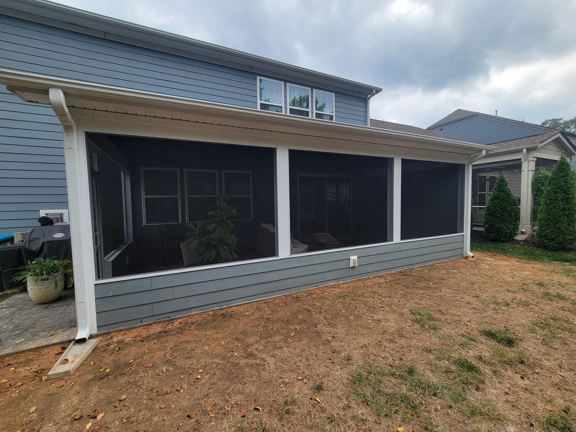 Screened porch addition on a blue house with white trim and a sloped roof over a gravel yard.