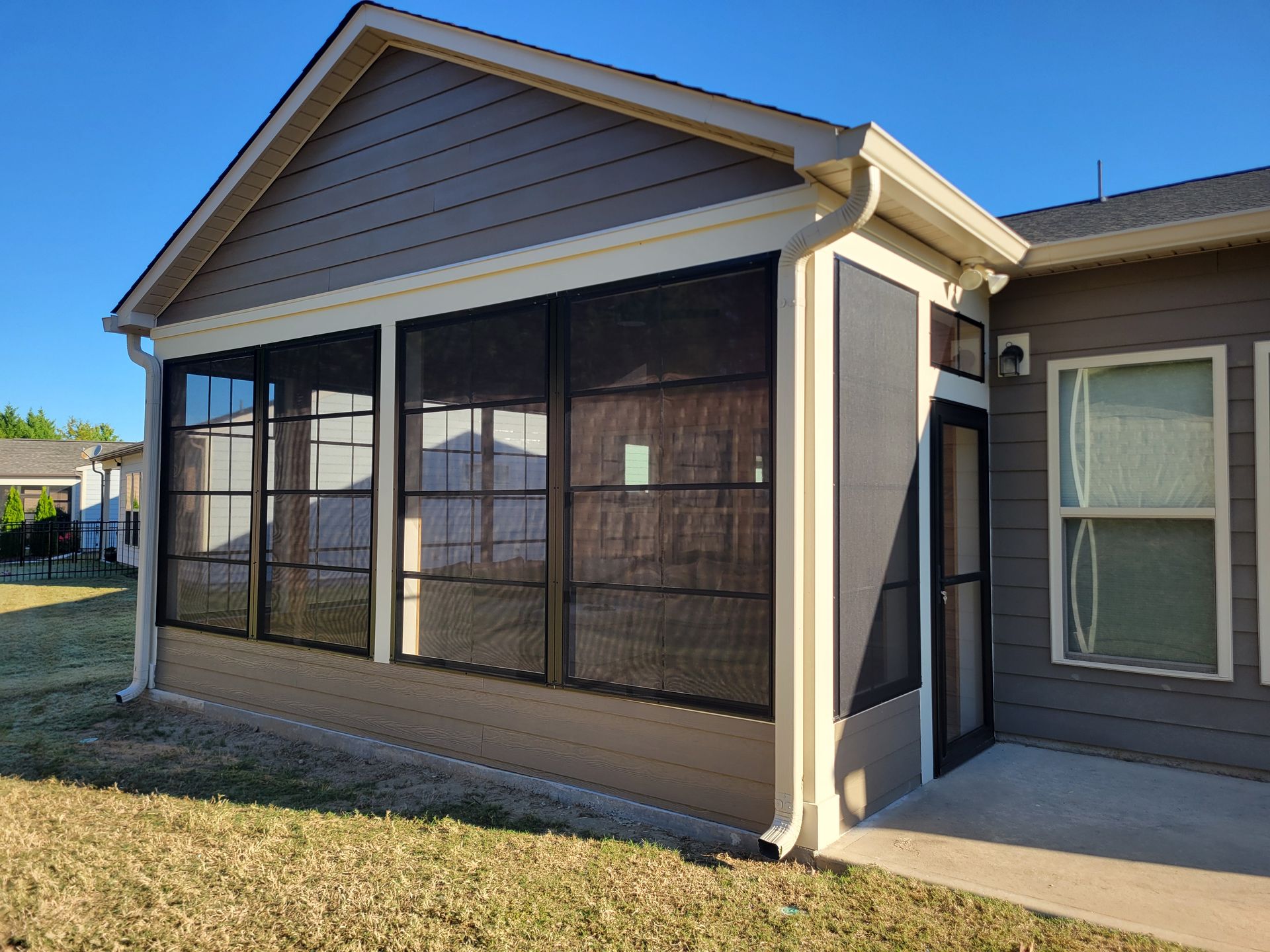 Screened porch with dark mesh windows and beige siding on a house in daylight