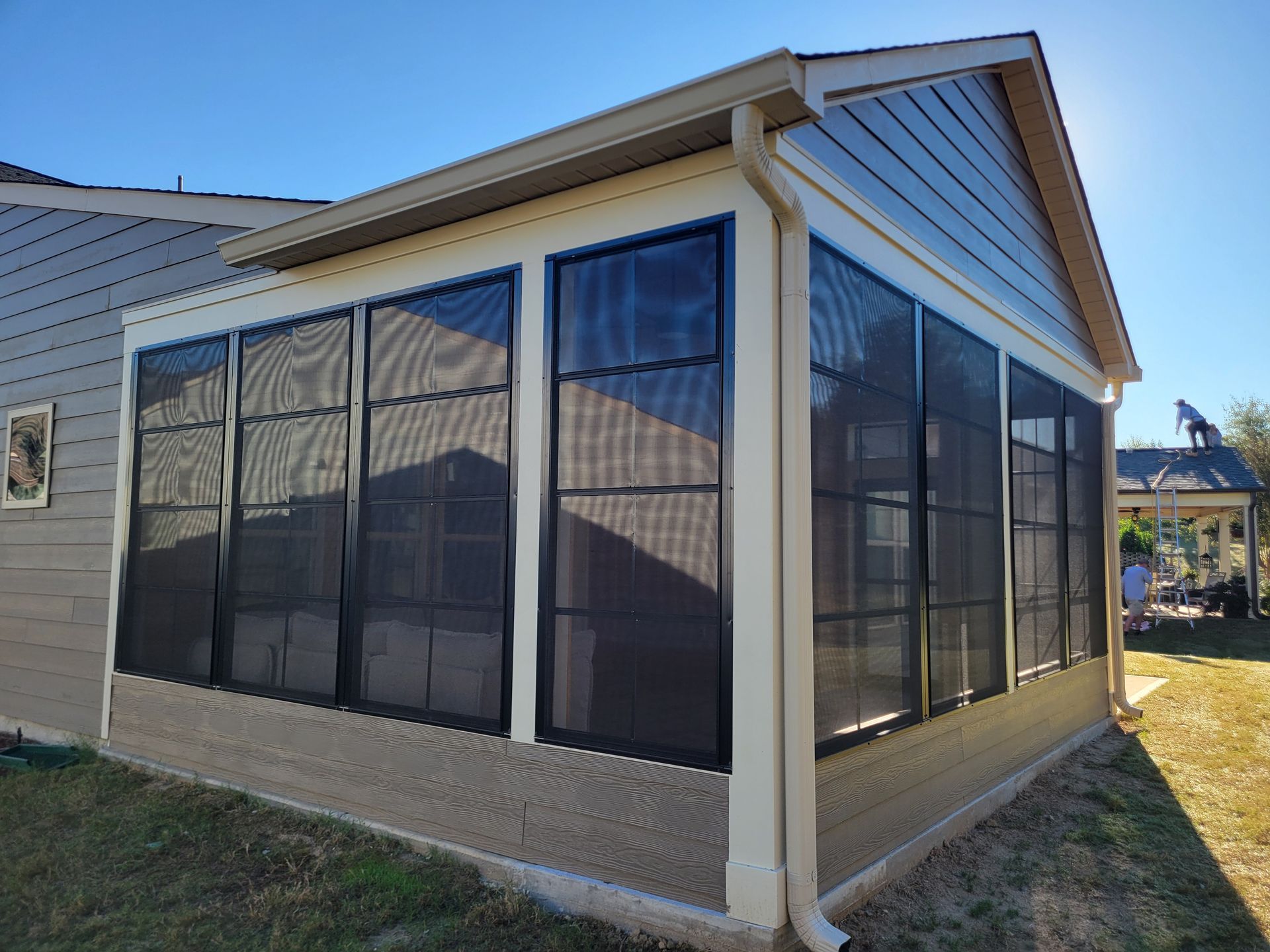 Screened porch on a beige house with white trim and dark mesh windows.