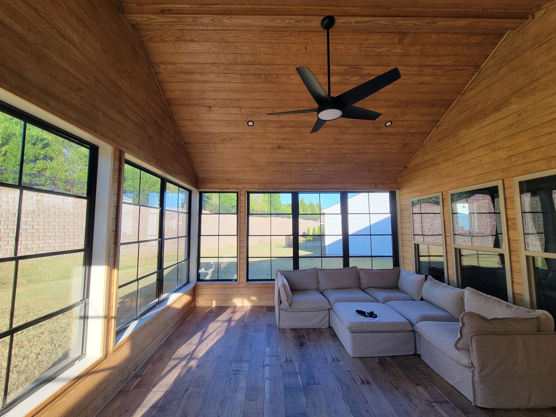 Sunroom with wood ceiling, large windows, sectional sofa, and ceiling fan in warm sunlight