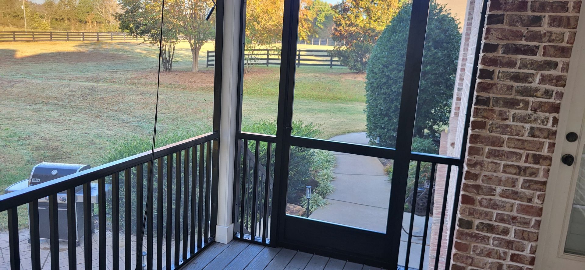 Porch with black railing and screen door overlooking a grassy yard at sunset