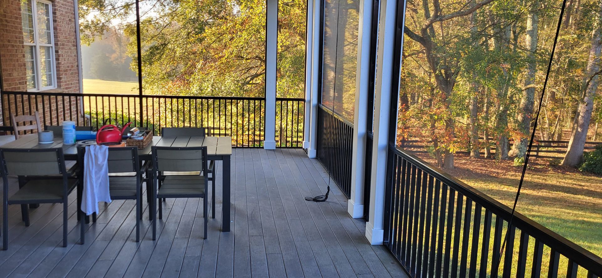 Wooden deck with patio table and chairs overlooking autumn trees and a black railing