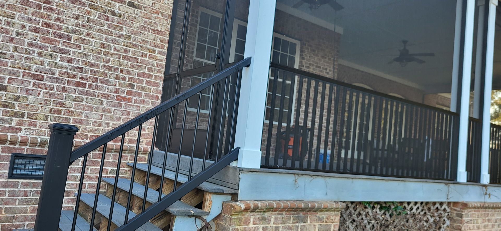 Brick house porch with black railing, steps, and a covered entry.
